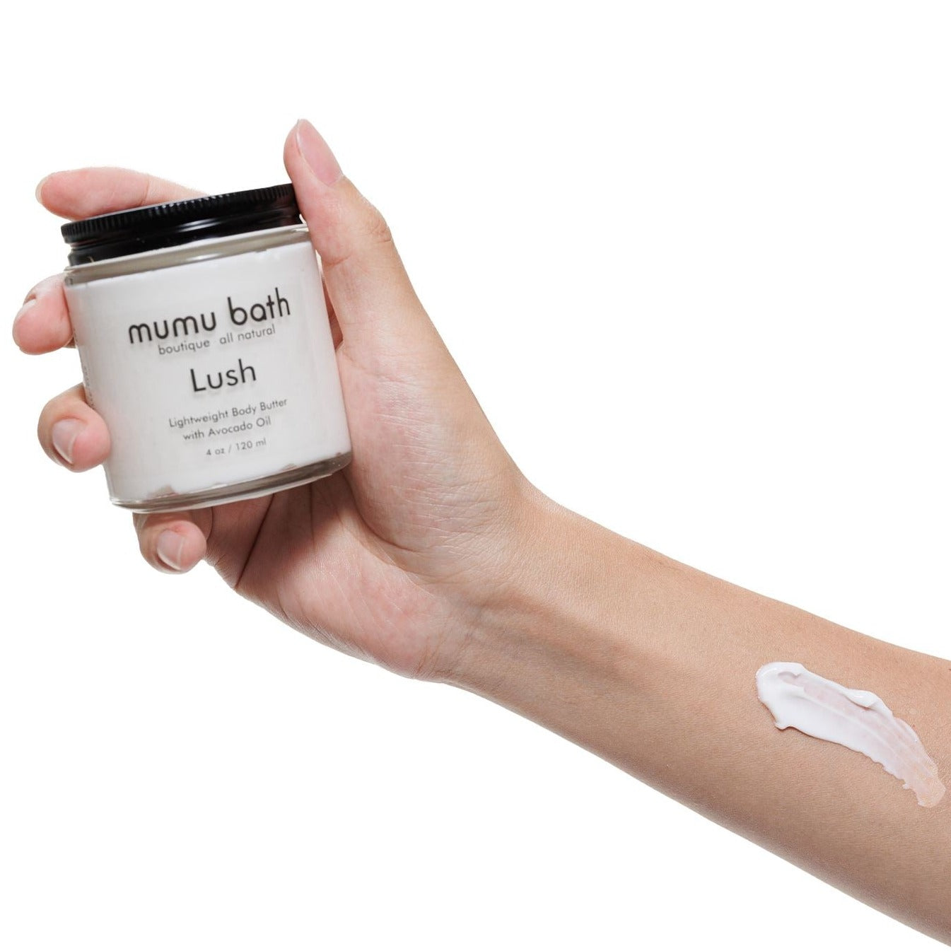 Hand holding a jar of Mumu Bath Lush Lightweight Body Butter with Avocado Oil, with a small amount of cream applied on the forearm